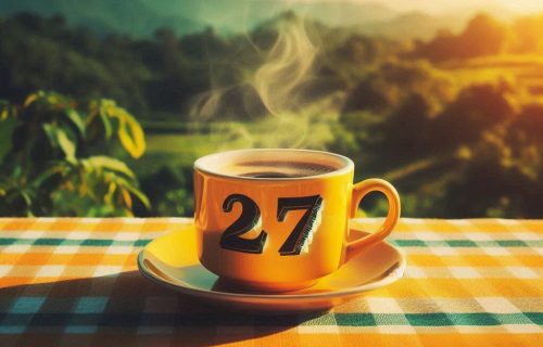 una taza de café humeante amarilla con el número 27 grabado en ella, sobre una mesa con mantel de cuadros colores amarillo verde azul naranja y con fondo de cielos naturales