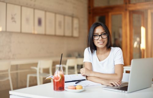 Young asian entrepreneur student working on laptop in library or open space cafe looking at camera smiling. Young asian entrepreneur student working on laptop in library or open space cafe looking at camera